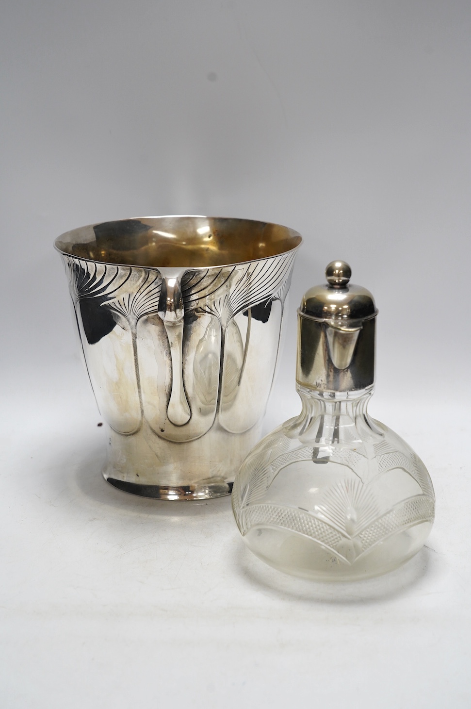 An Art Nouveau Orivit polished pewter wine cooler, c.1905, impressed model number 2447, 20cm high, and an early 20th century WMF electroplate mounted cut glass claret jug, 21.5cm high (2). Condition - fair to good